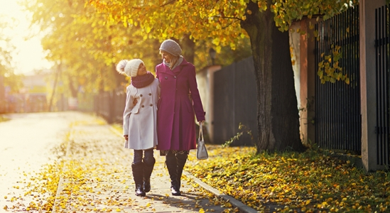 Mother and daughter strolling on a sidewalk dusted with leaves looking at each other