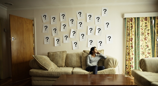 Woman sitting on couch with question marks plastered on the wall behind her