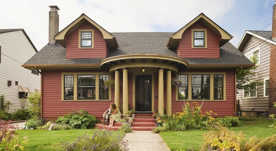 Wide shot of a red house with a woman and dog sitting on the front steps