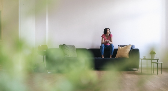 Wide angle shot of a woman sitting on her couch looking off into the distance